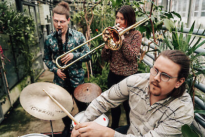 Pressefoto Bonsai, spielend (vlnr: Bassclarinette, Posaune, Drums), im Hintergrund Pflanzen